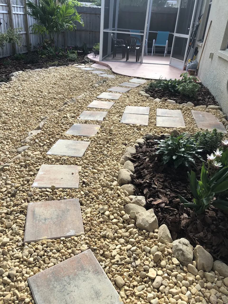 Flagstone stepping stones through river rock beside a screen enclosure
