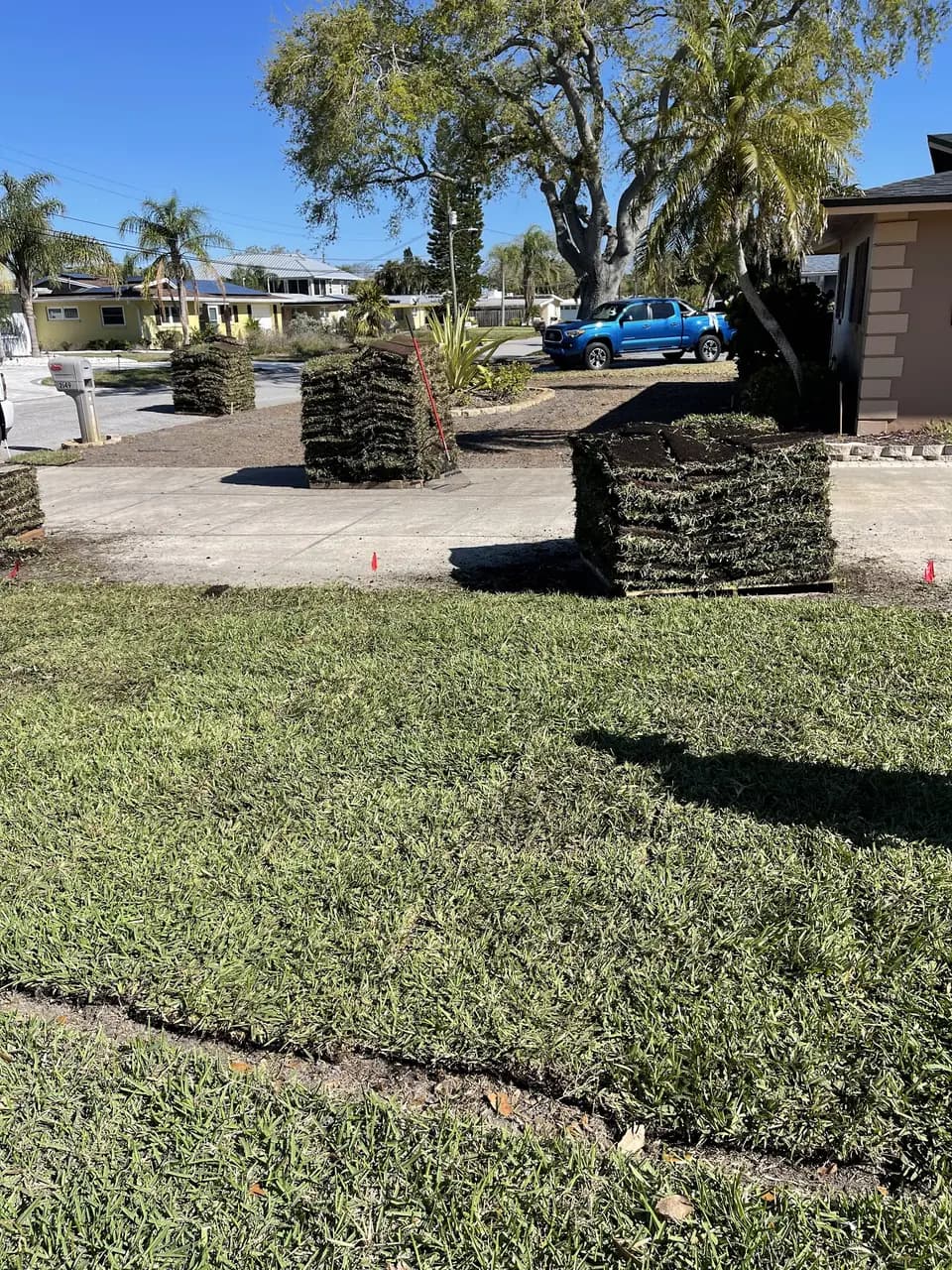 Freshly laid sod with more rolls stacked at the curb