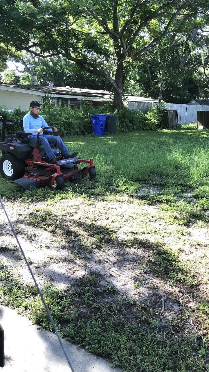 Crew member mowing a lawn under shade trees