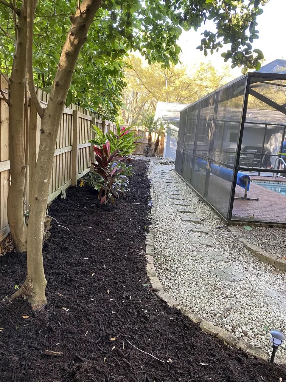 Dark mulch bed beside a white rock path along a screened pool cage